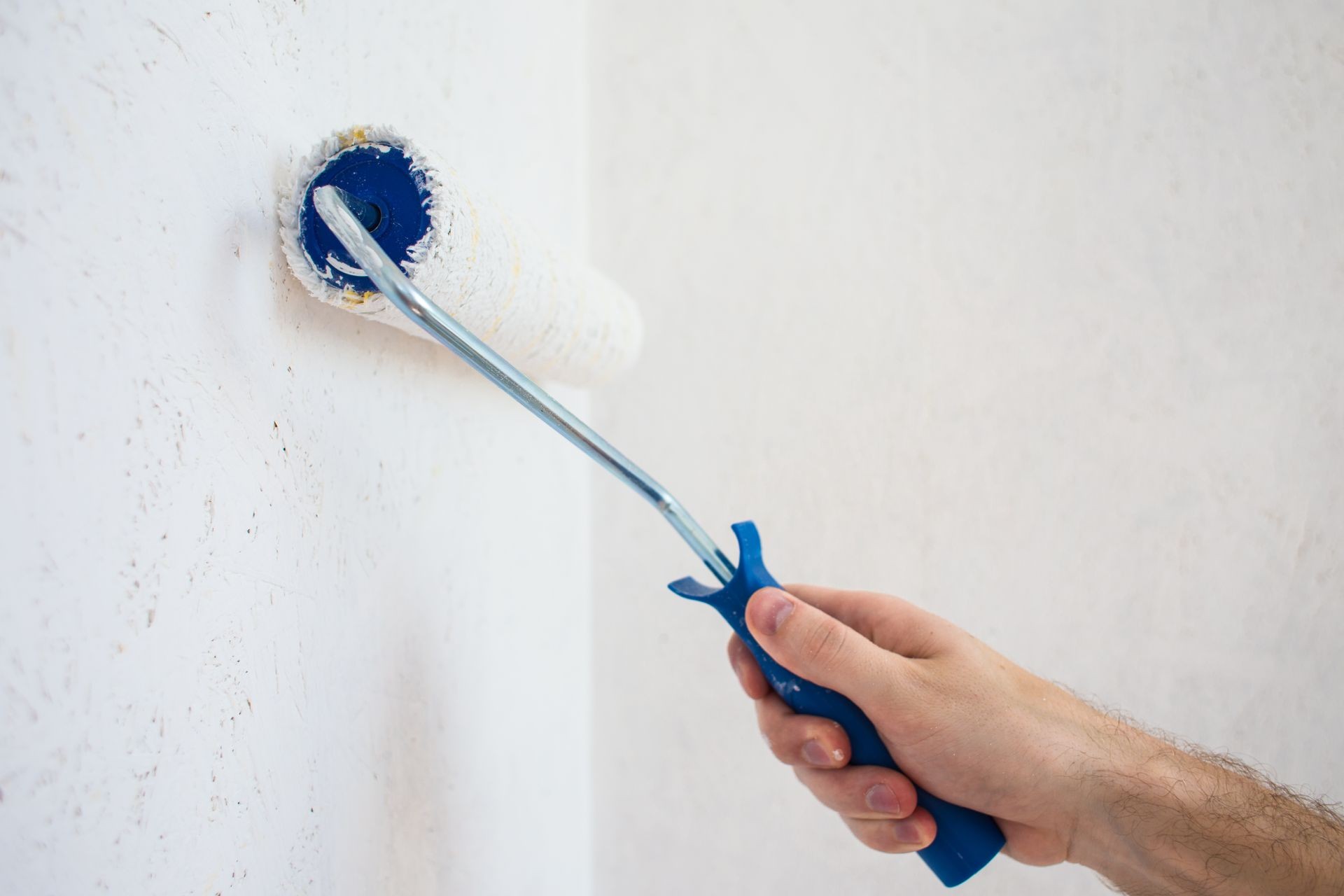The worker's hand paints the wall with a roller in white color